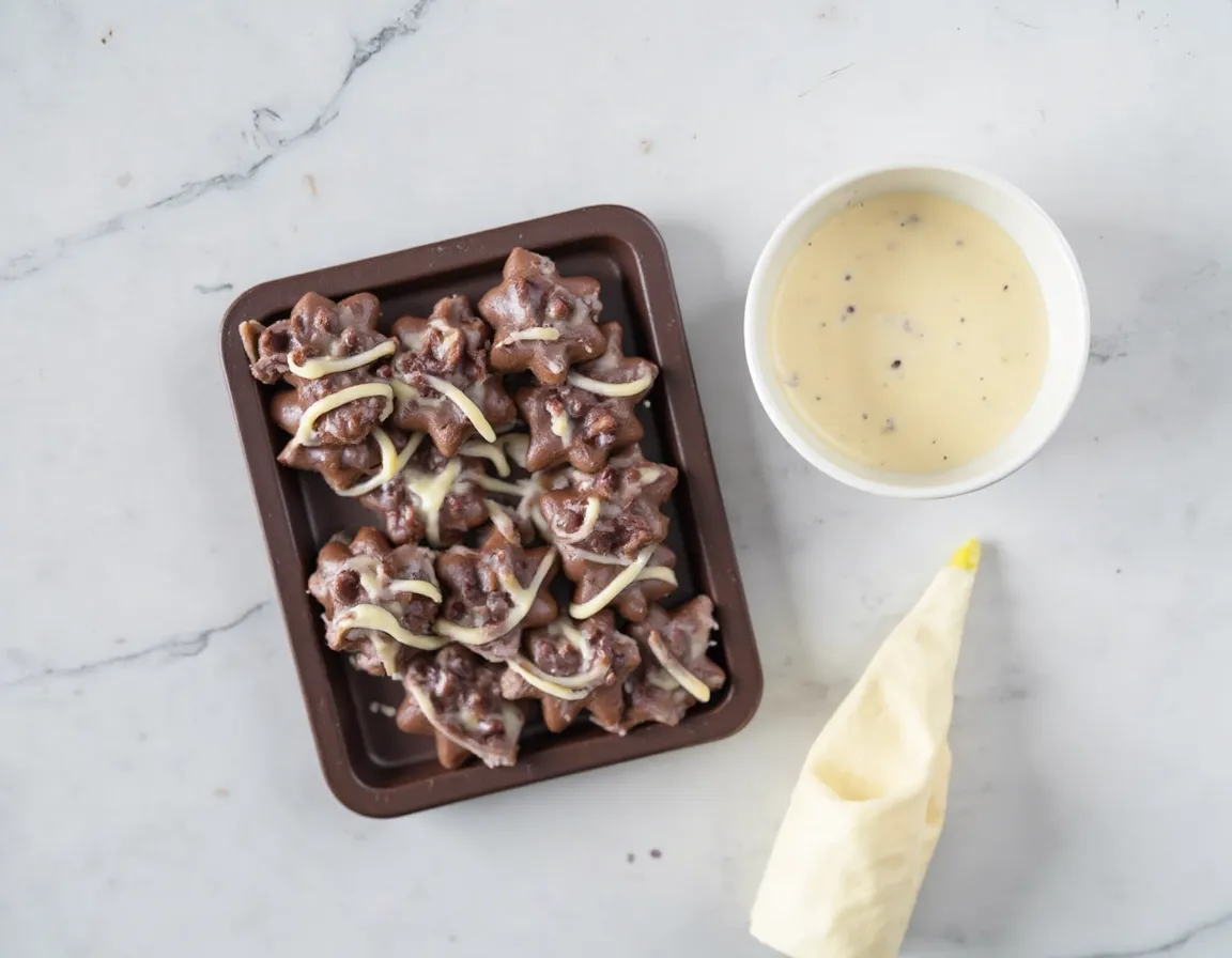 Silikonform mit dekorativen weißen Schokoladenlinien und Wirbelmustern auf dem Formboden neben einem Spritzbeutel