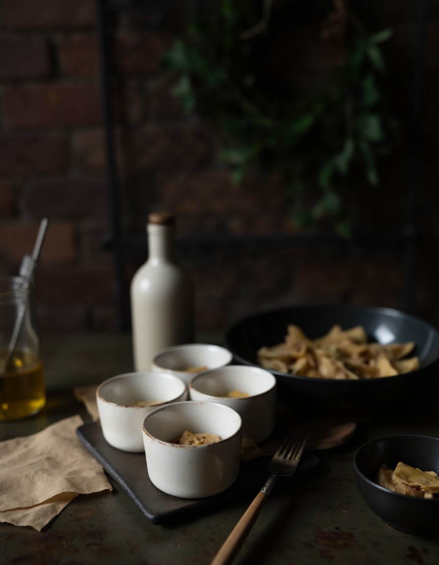 Vier eingeölte weiße Ramekins neben einem Stapel Wonton-Blätter und der fertigen Dumpling-Füllung bereit zum Schichten