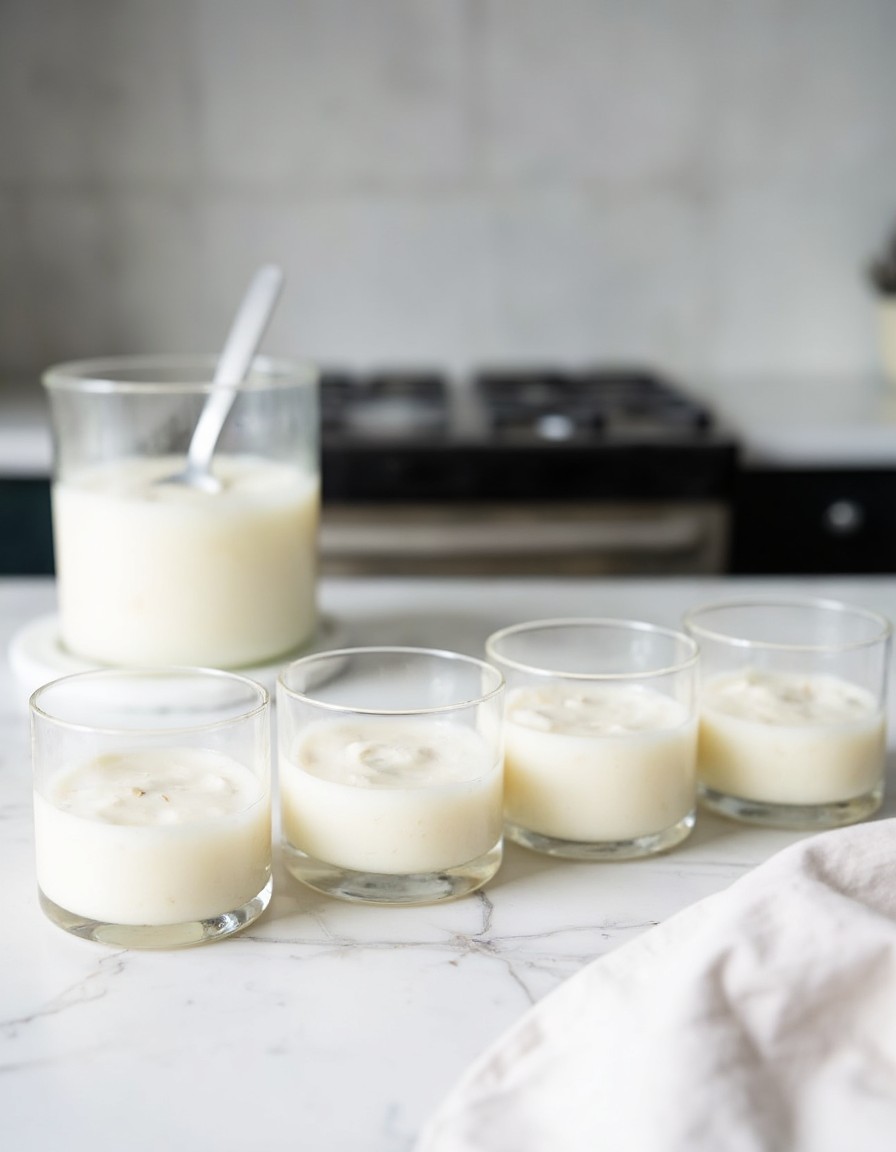 Vier Dessertgläser in einer Reihe auf Marmorplatte, jeweils gefüllt mit glattem weißem griechischem Joghurt